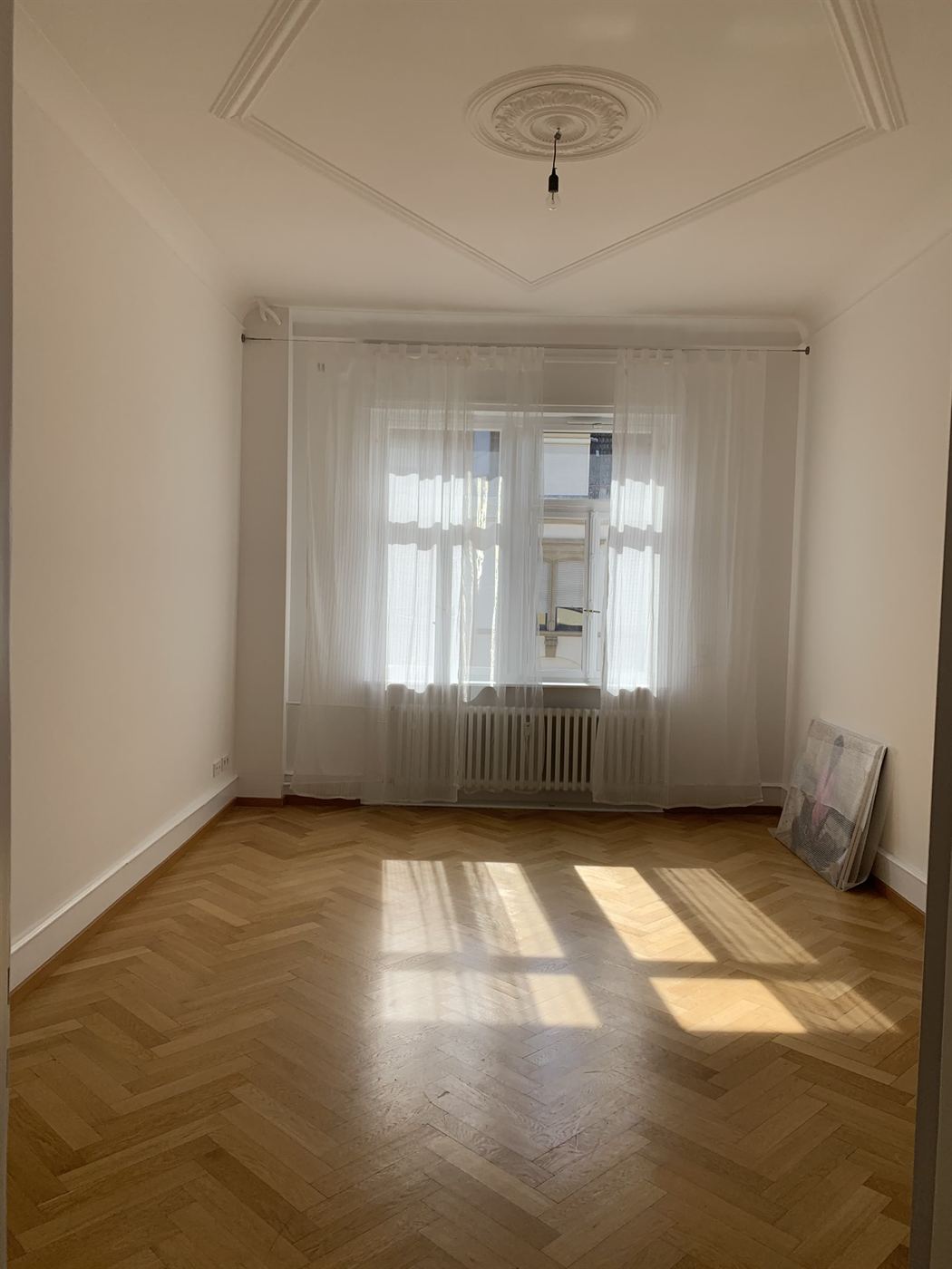 Wohnzimmer mit Fischgrätparkett und matten weißen Wänden im renovierten Altbau